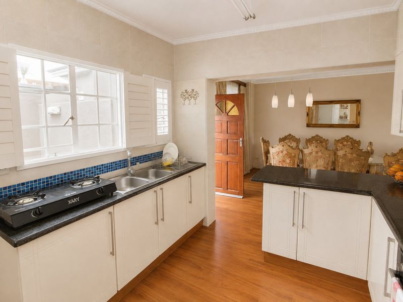 Open plan kitchen and dining area featuring granite countertops, shaker-style cabinetry, gas cooktop, and warm laminate flooring with direct access to the home entrance.