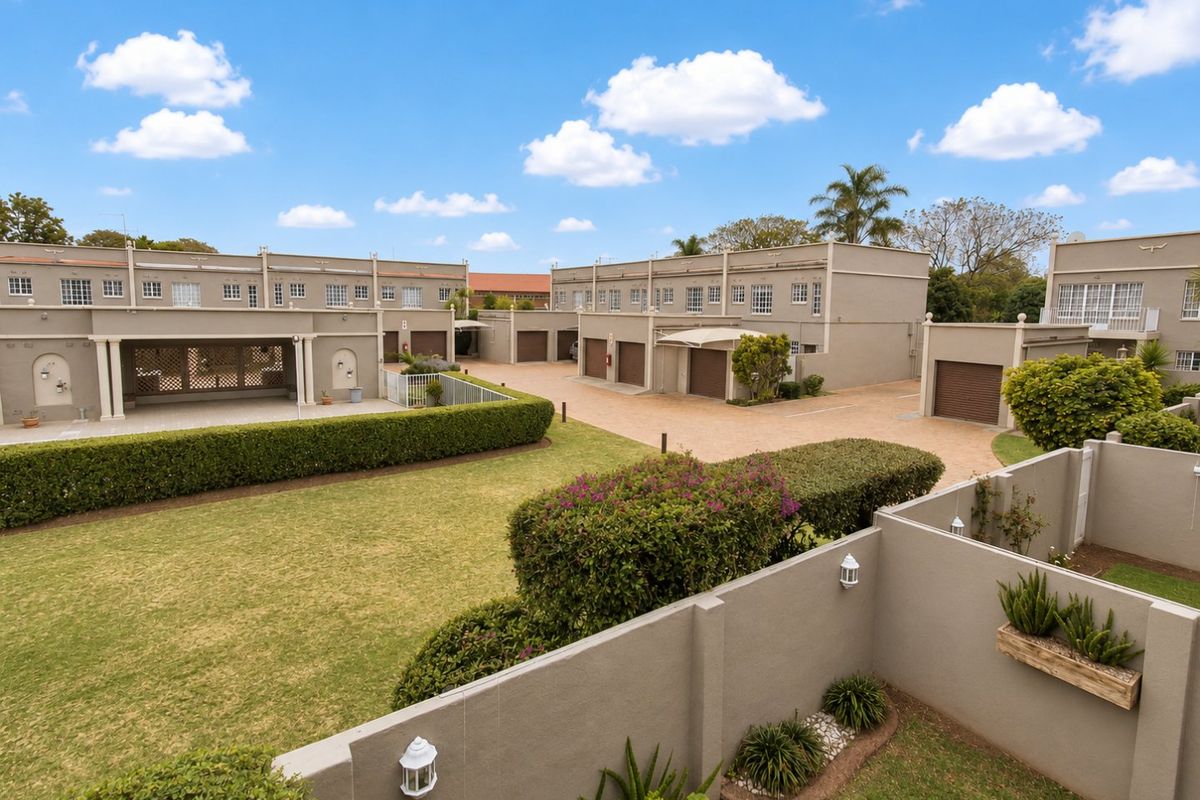 An elevated view of a townhouse complex featuring a shared paved driveway, multiple garage units, and well-maintained communal garden areas with boundary walls.