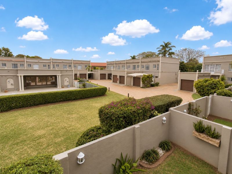An elevated view of a townhouse complex featuring a shared paved driveway, multiple garage units, and well-maintained communal garden areas with boundary walls.