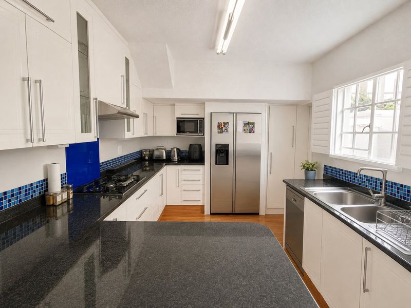 Modern kitchen featuring white shaker cabinetry, dark granite countertops, blue mosaic tile splashback, gas hob, and integrated appliances.