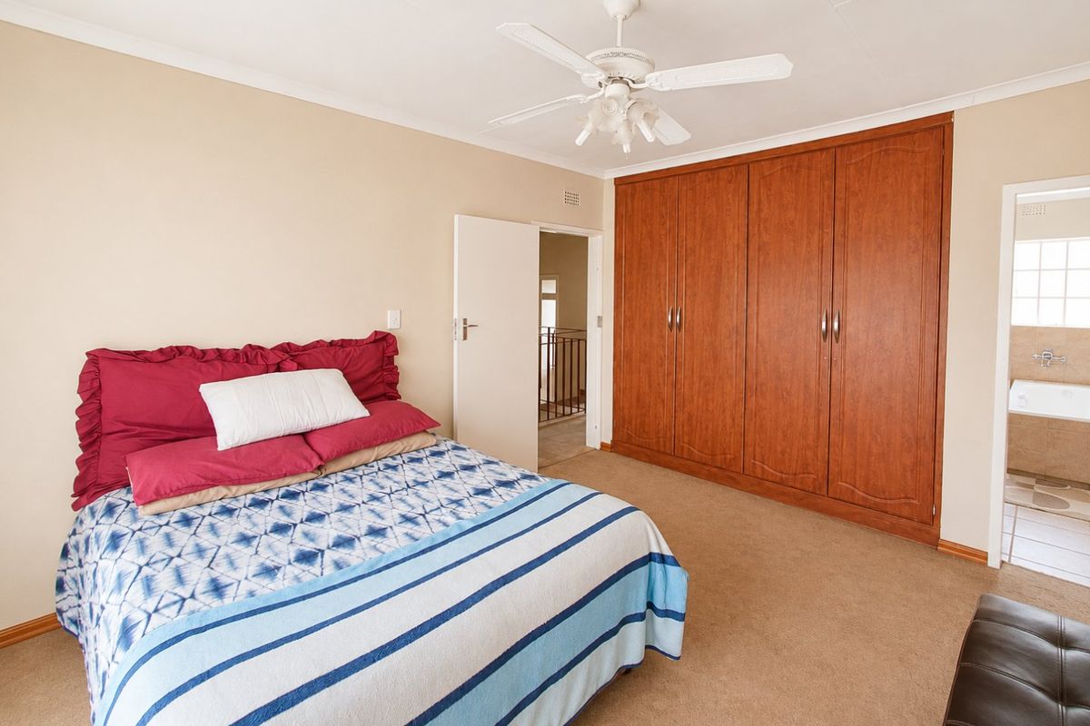Spacious bedroom featuring built-in wooden cupboards, a ceiling fan, and neutral carpeting, with direct access to an en-suite bathroom.