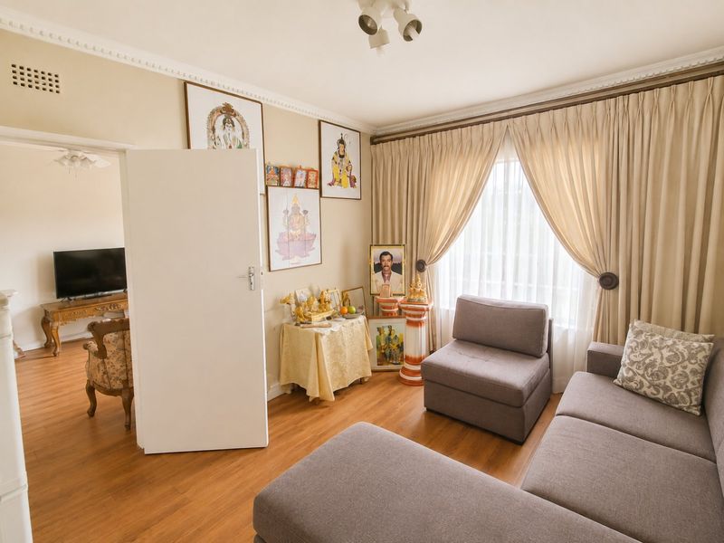 A living room featuring laminate flooring, decorative ceiling cornices, and a large window with curtains, providing a comfortable and functional living space.
