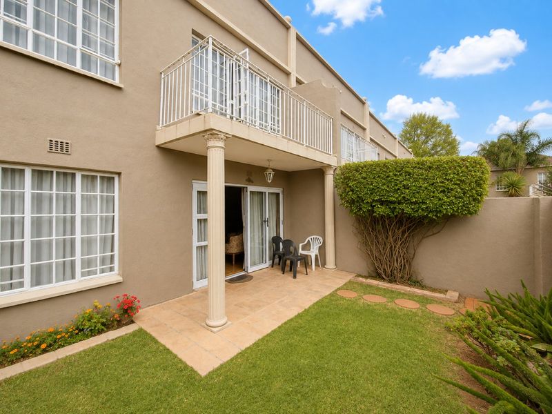 Rear view of the townhouse featuring a tiled patio, a balcony with classical columns, and a private landscaped garden area.