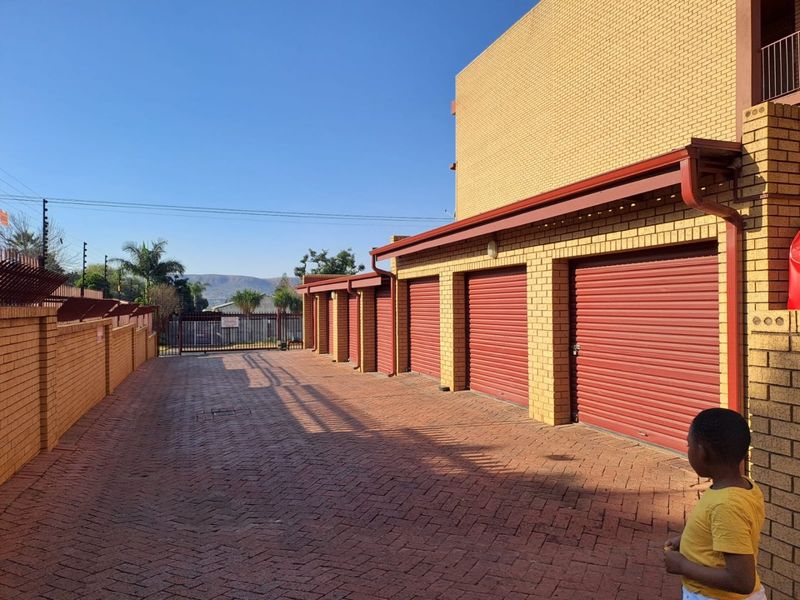 Exterior view of a residential apartment complex featuring a paved driveway with multiple red roller shutter garage doors and secure perimeter fencing.