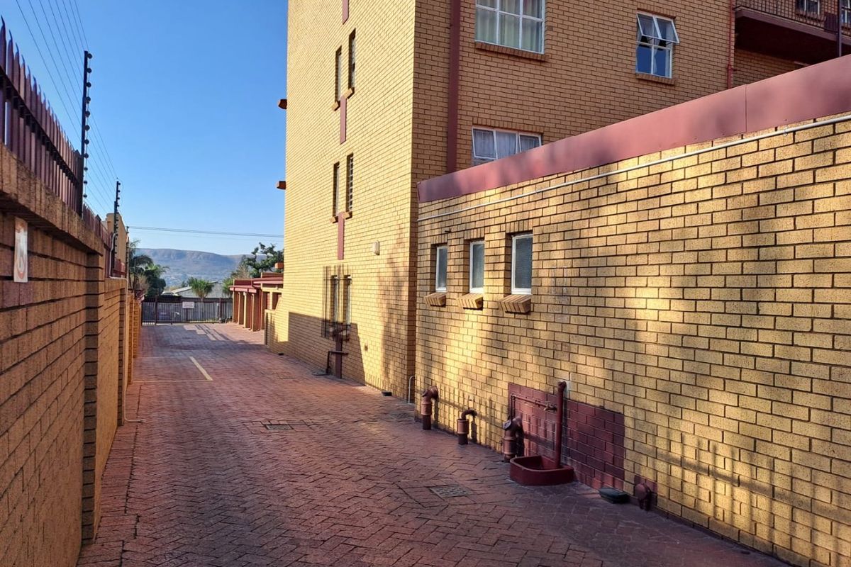A view of the paved rear exterior area of the apartment complex, featuring face brick walls and secure perimeter fencing.