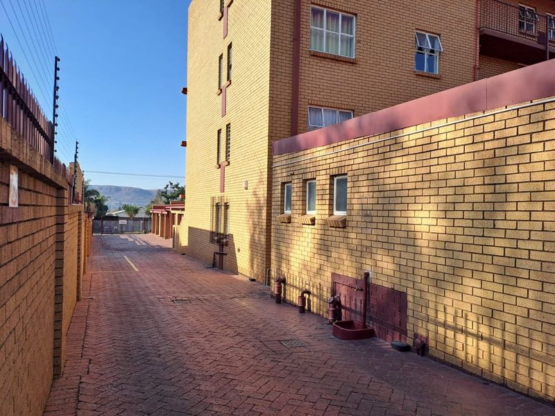 A view of the paved rear exterior area of the apartment complex, featuring face brick walls and secure perimeter fencing.