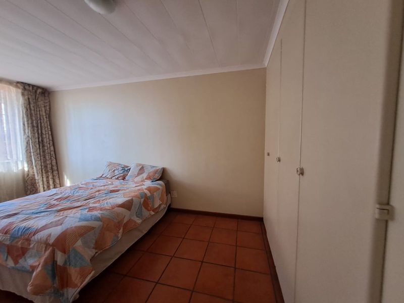 A bedroom featuring built-in cupboards, tiled flooring, and a panelled ceiling, offering a functional space with neutral finishes.