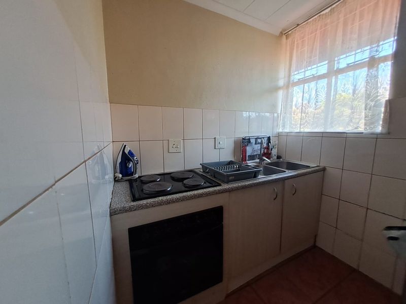Compact kitchen featuring a built-in oven, electric hob, stainless steel sink, and tiled splashback, offering a functional layout with potential for modern updates.