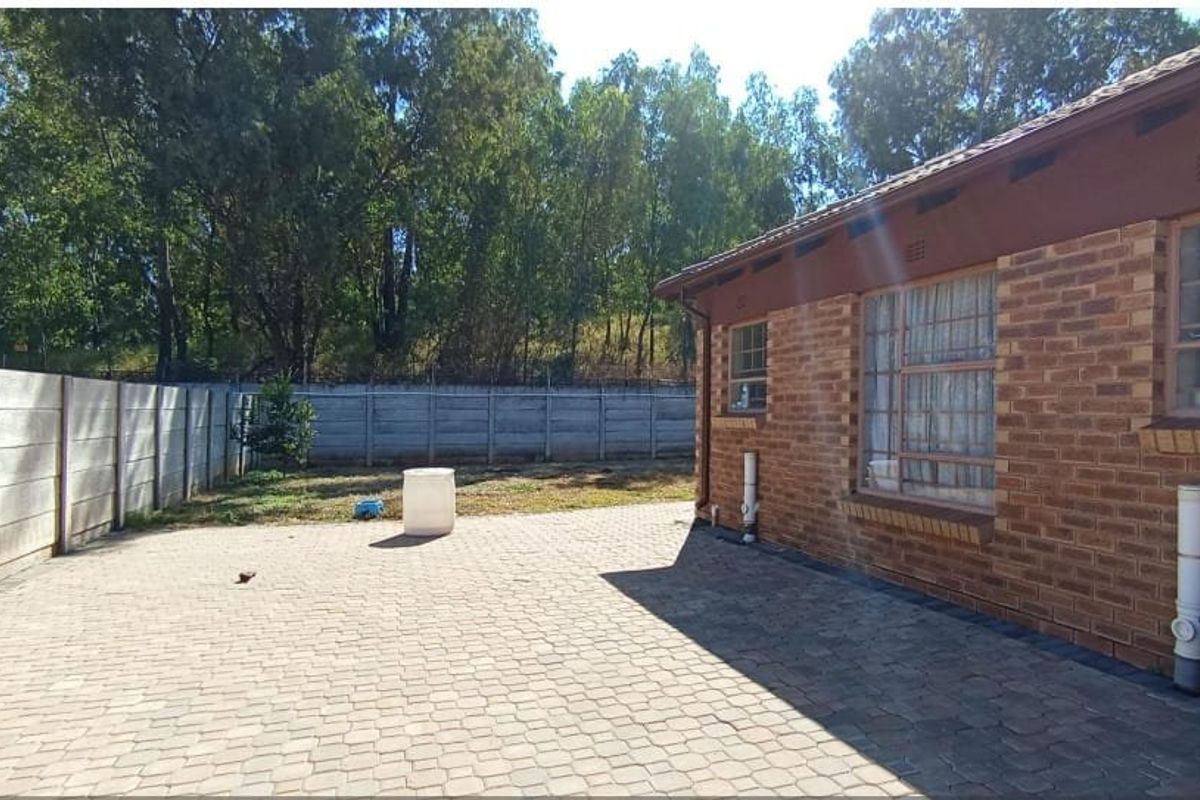 Rear exterior view of the property featuring a paved patio area, brick facade, and a secure precast concrete boundary wall.