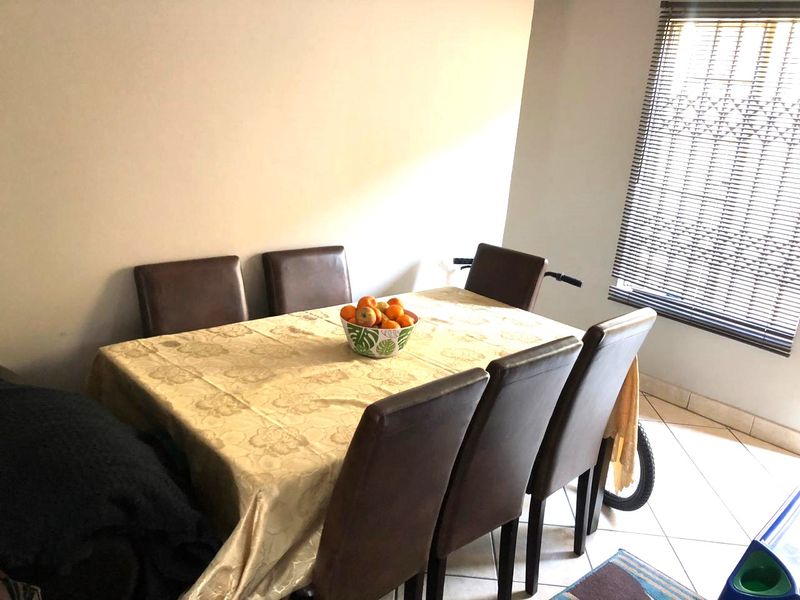 A functional dining area featuring tiled flooring and a window fitted with venetian blinds and a security gate.
