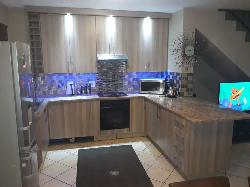 A functional kitchen featuring wood-finish cabinetry, granite countertops, a mosaic tile backsplash, and integrated appliances including an oven and hob.