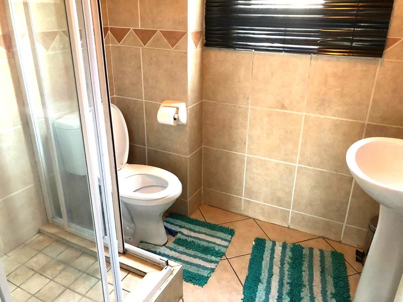 A functional bathroom featuring a shower enclosure, pedestal basin, and toilet with neutral ceramic tiling throughout.