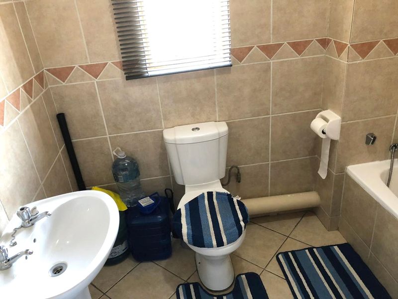 A functional bathroom featuring a pedestal basin, toilet, and bathtub with neutral wall tiling and a window with a venetian blind.