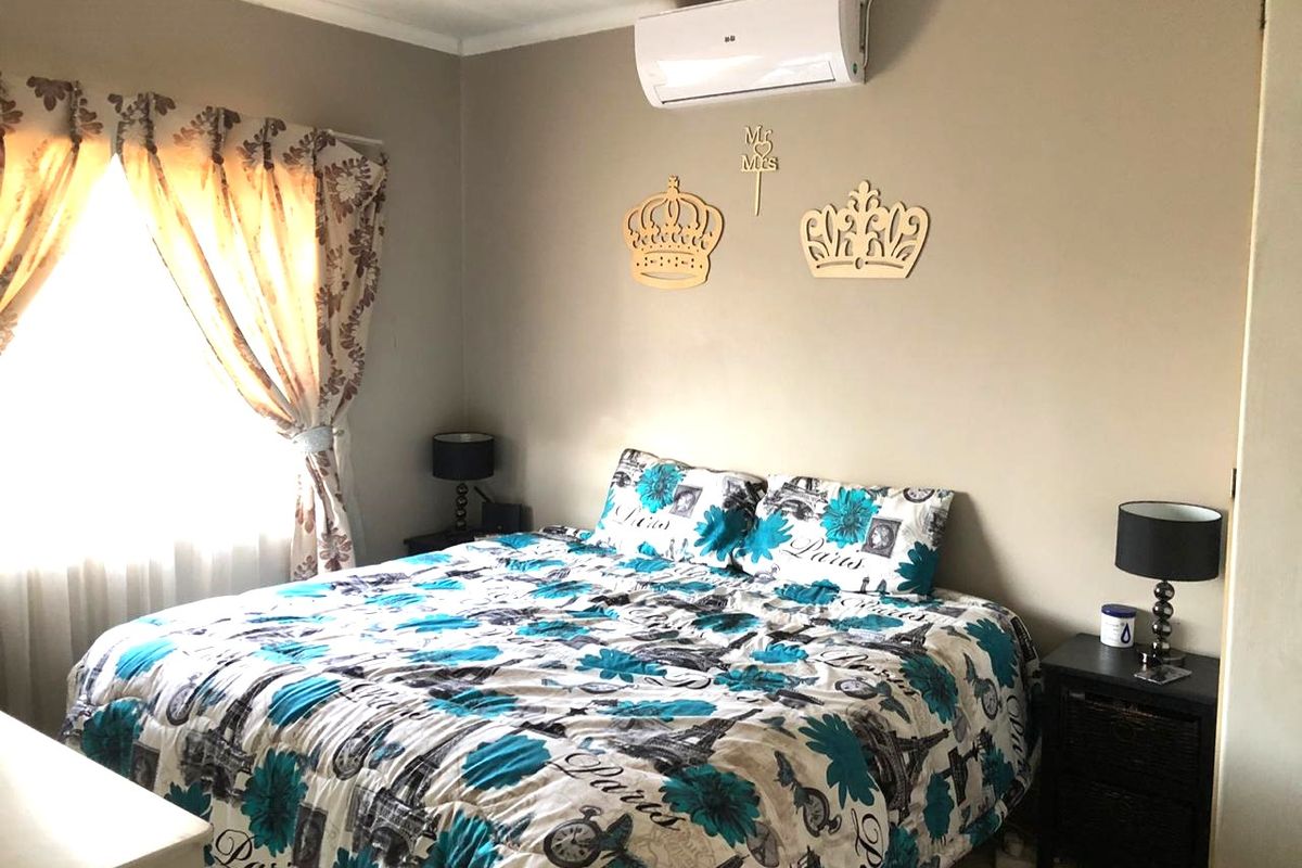 A bedroom featuring a wall-mounted split-system air conditioning unit and natural light through a window with curtain rails.