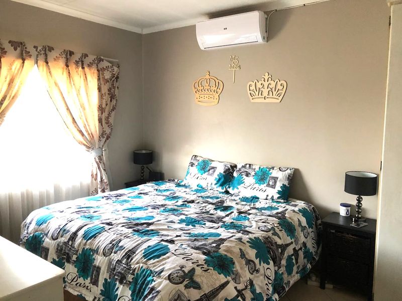 A bedroom featuring a wall-mounted split-system air conditioning unit and natural light through a window with curtain rails.