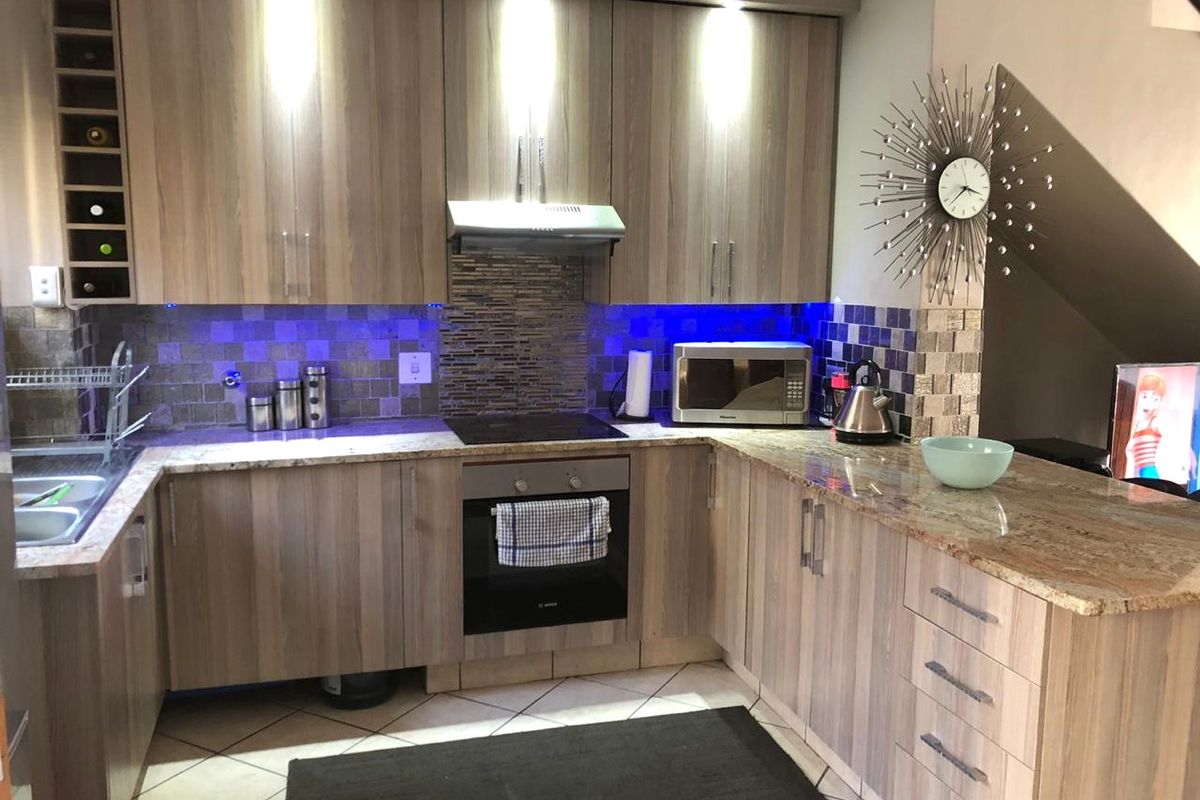 Modern kitchen featuring wood-grain cabinetry, granite countertops, mosaic tile backsplash, and integrated appliances with under-cabinet accent lighting.