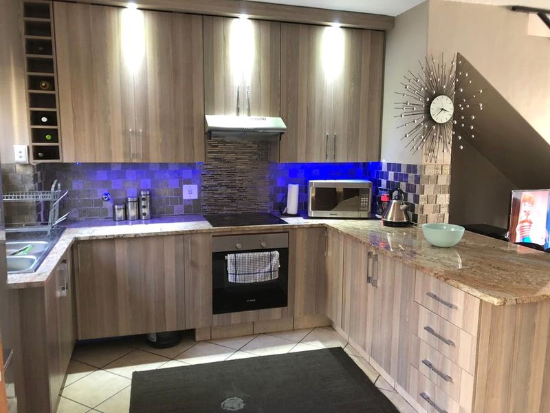 Modern kitchen featuring wood-grain cabinetry, granite countertops, mosaic tile backsplash, and integrated appliances with under-cabinet accent lighting.