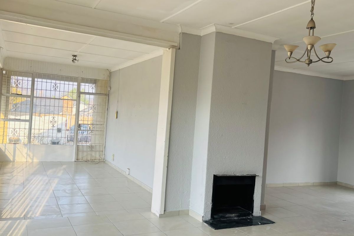 Spacious, empty living area featuring a central fireplace, tiled flooring, and large windows with security bars, offering a bright and open layout.