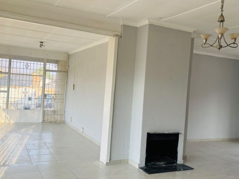 Spacious, empty living area featuring a central fireplace, tiled flooring, and large windows with security bars, offering a bright and open layout.