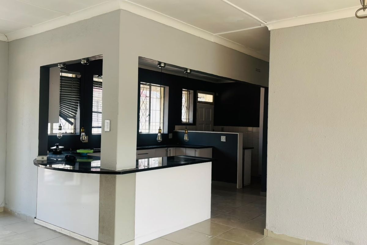 A clean, open-plan kitchen featuring a breakfast bar, granite countertops, and modern pendant lighting, offering a functional and well-lit cooking space.