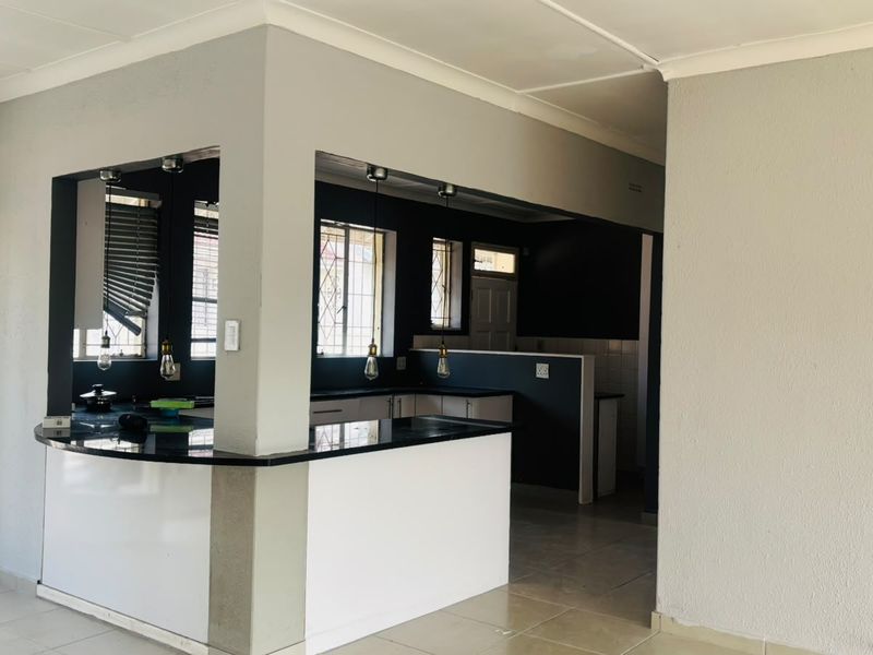 A clean, open-plan kitchen featuring a breakfast bar, granite countertops, and modern pendant lighting, offering a functional and well-lit cooking space.