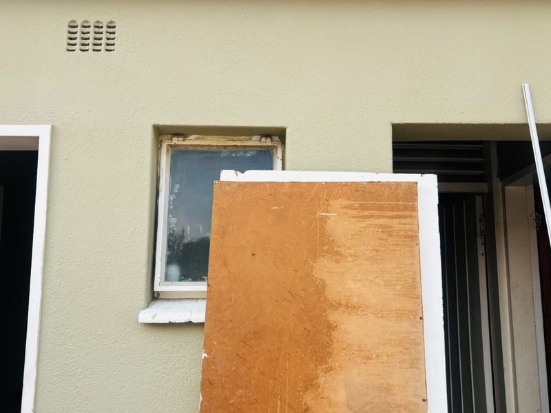 Exterior view of a building facade showing window and door frames with visible signs of weathering and maintenance requirements.