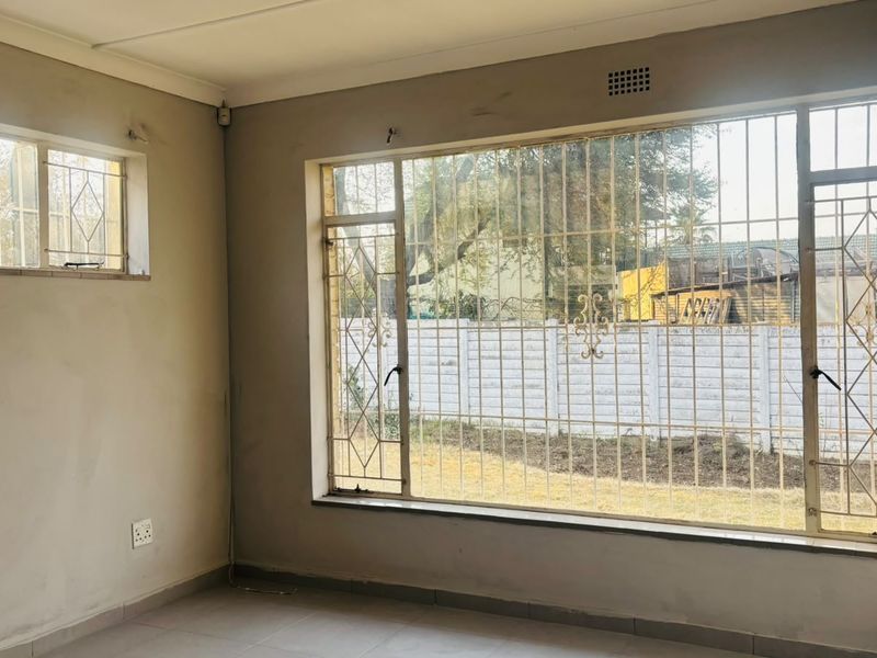 An empty living room featuring large windows with security bars, tiled flooring, and neutral walls, offering a blank canvas for renovation.