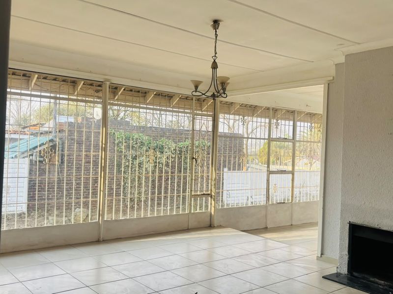 Spacious living area featuring tiled flooring, a built-in fireplace, and large windows with security bars, offering a bright and open layout.
