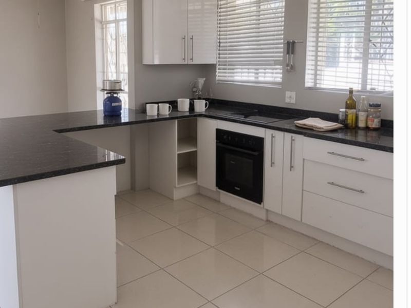 A functional kitchen featuring white cabinetry, dark granite countertops, built-in oven, and neutral ceramic floor tiles with ample natural light.