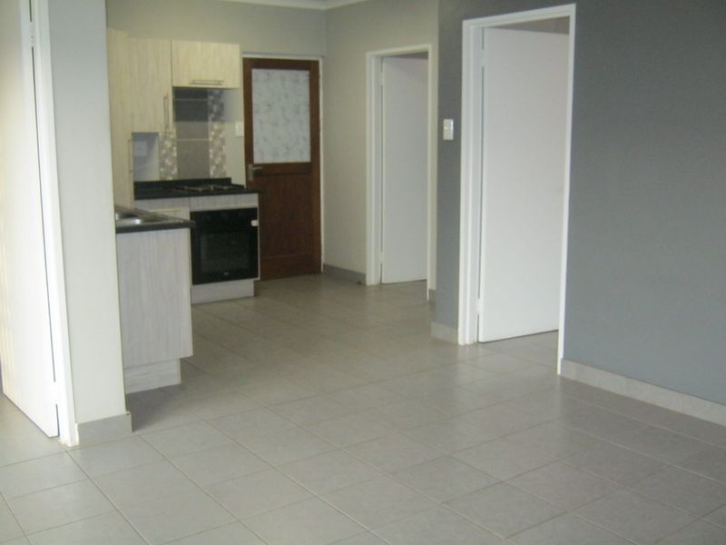 An open-plan living area featuring tiled flooring and a compact kitchen with built-in cabinetry, oven, and hob.