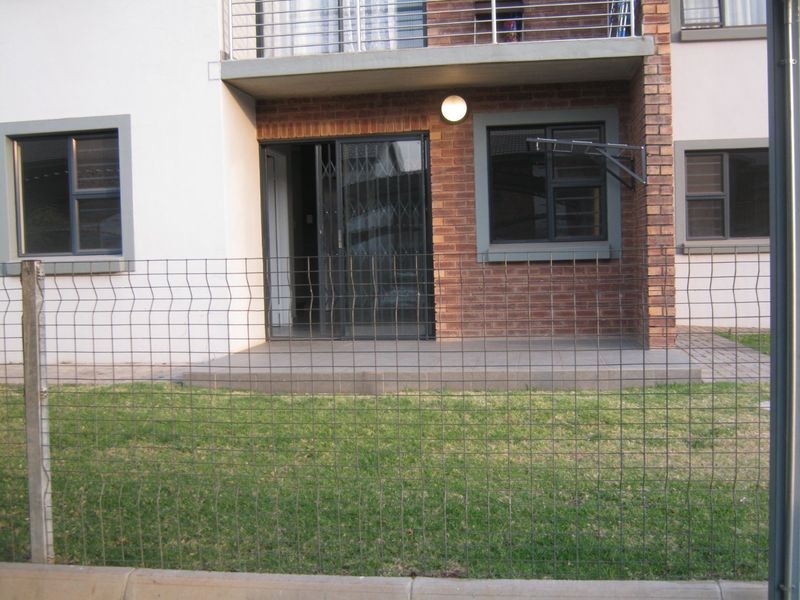 Ground floor apartment exterior featuring a tiled patio, sliding glass door with security gate, brick facade, and an upper-level balcony with metal railing.