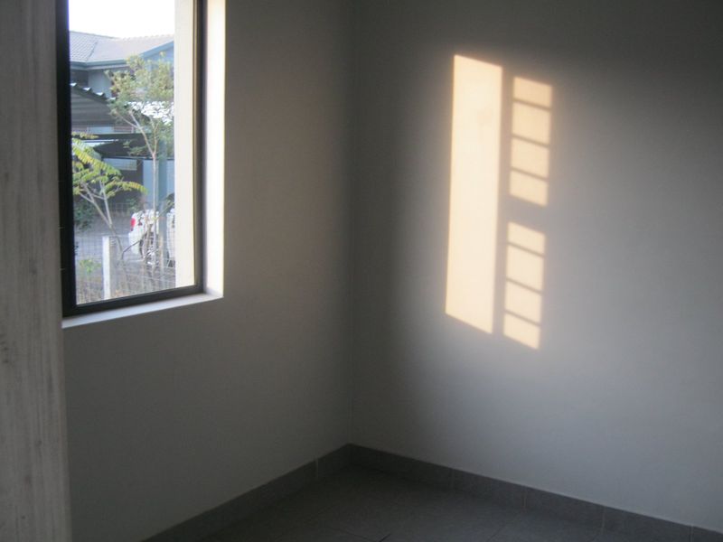 A vacant bedroom featuring tiled flooring and a window with an aluminium frame, receiving natural light.