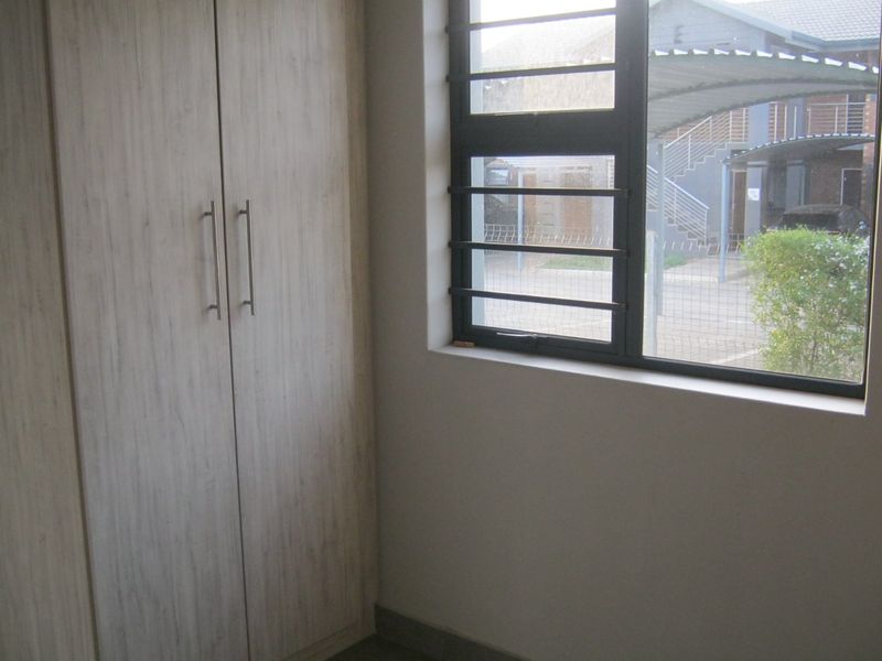 A bright bedroom featuring a built-in wardrobe with light wood-grain finish and a window fitted with security bars.