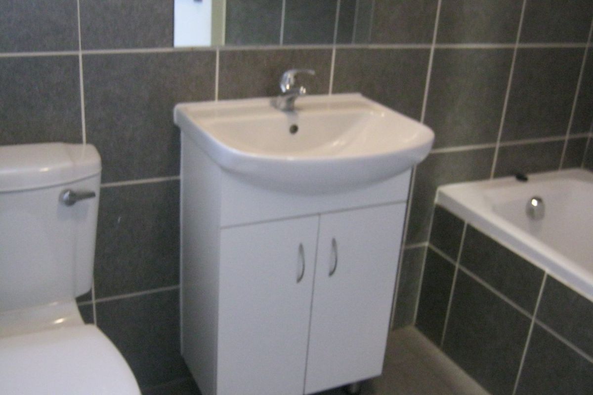 A functional bathroom featuring a white vanity cabinet with basin, toilet, and bathtub, finished with dark grey wall tiles.