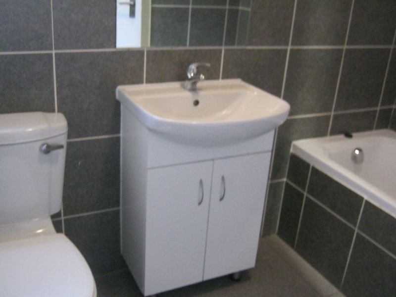 A functional bathroom featuring a white vanity cabinet with basin, toilet, and bathtub, finished with dark grey wall tiles.