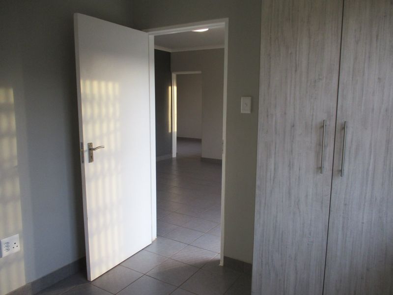 A clean, empty hallway featuring tiled flooring and built-in cupboards, providing access to adjacent rooms within the apartment.
