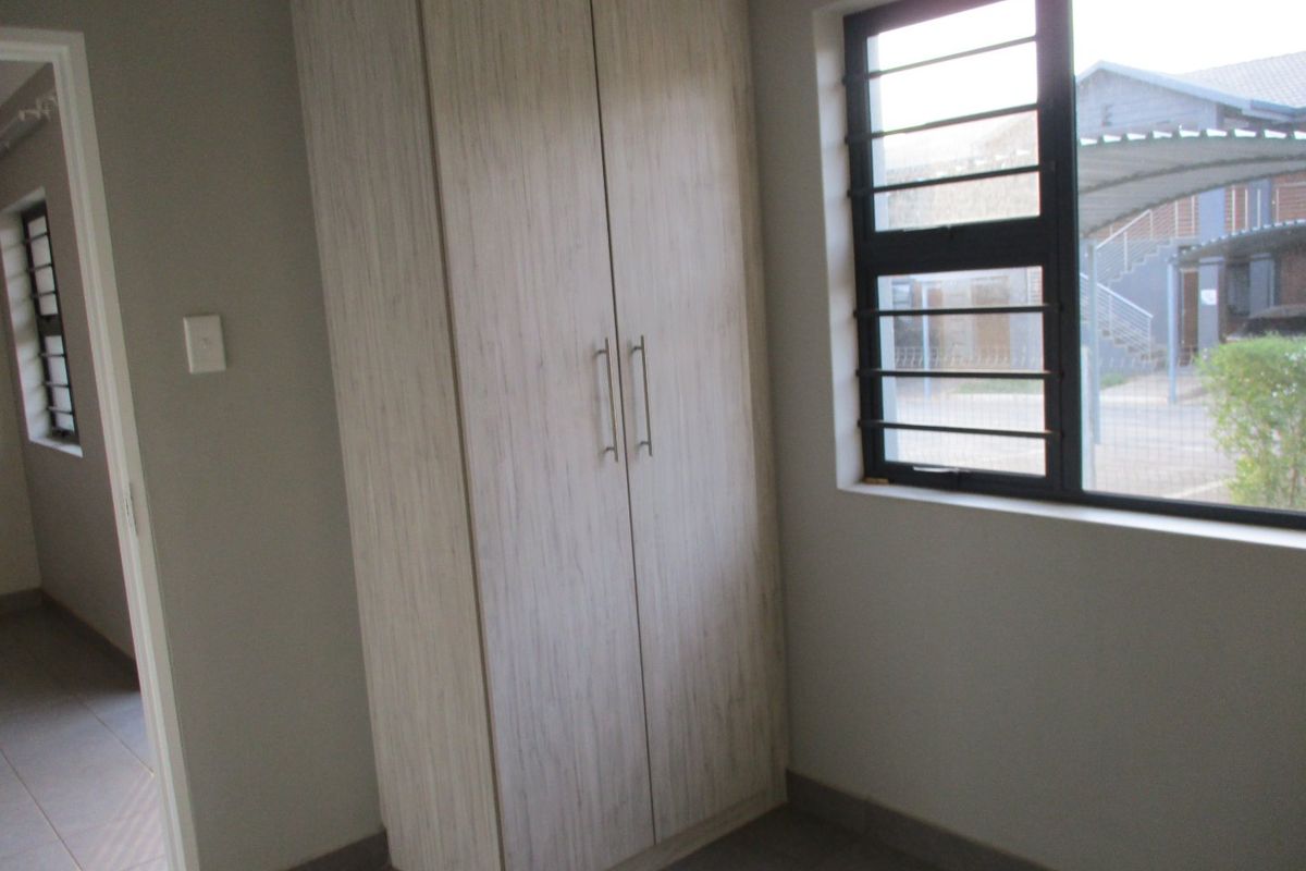 A clean, empty bedroom featuring neutral tiled flooring, a built-in wardrobe, and windows fitted with security bars.