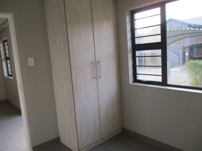 A clean, empty bedroom featuring neutral tiled flooring, a built-in wardrobe, and windows fitted with security bars.