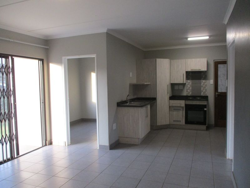 Open plan living area featuring a modern kitchen with built-in cabinetry, oven, hob, and tiled flooring, leading to an adjacent room.