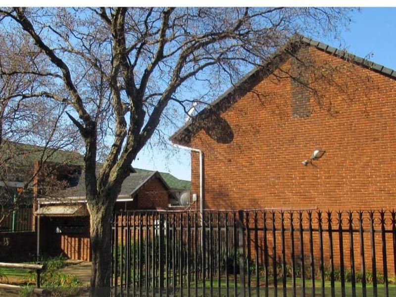 Rear view of the apartment building featuring exposed brickwork, tiled roofing, and secure perimeter metal fencing.