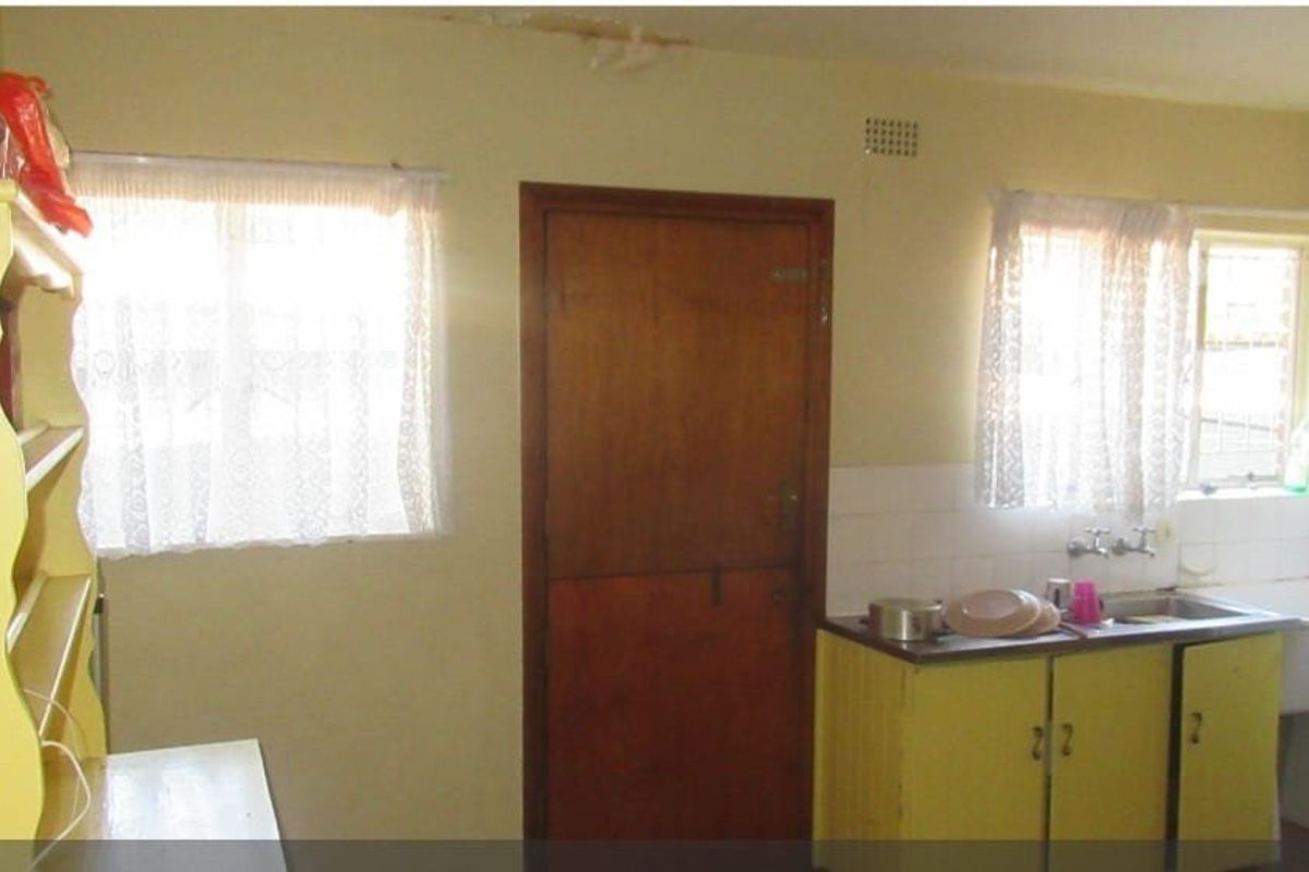 A dated kitchen area featuring basic cabinetry, a sink, and a separate laundry basin with tiled splashbacks.