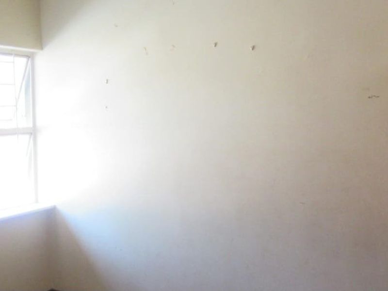 An empty bedroom featuring a window with security bars and walls showing signs of wear and surface imperfections.