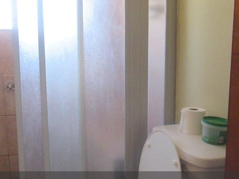 A compact bathroom featuring a shower enclosure with tiled walls and a standard toilet, requiring cosmetic updates to improve its dated appearance.