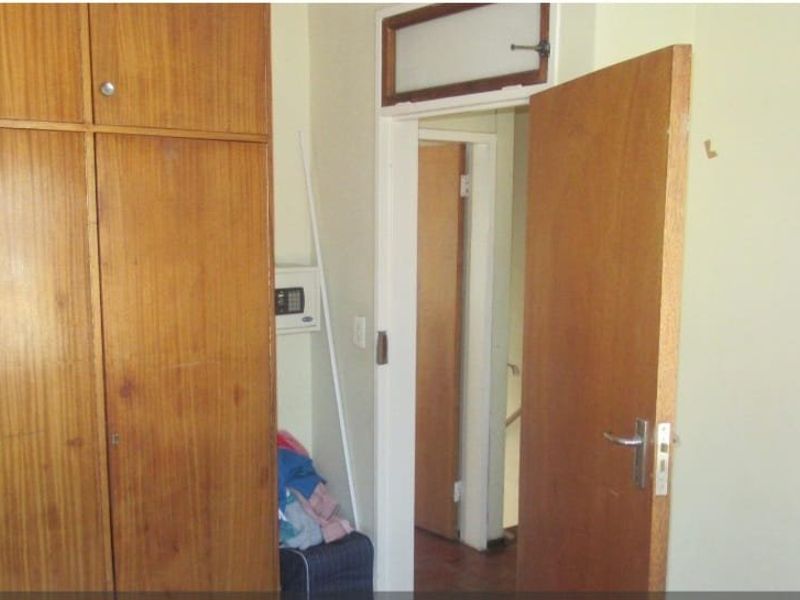 A bedroom featuring built-in wooden cupboards and a wooden door, showing signs of wear and dated finishes.