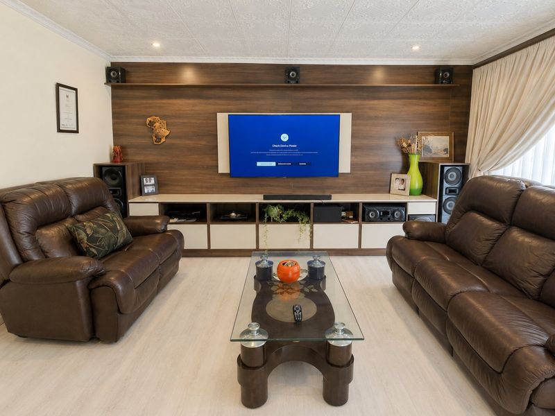 A well-maintained living room featuring a custom built-in media wall unit with integrated shelving and modern laminate flooring.
