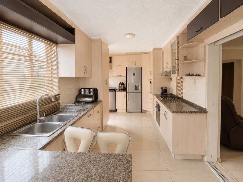 A well-maintained kitchen featuring light wood cabinetry, granite countertops, built-in appliances, and tiled flooring, offering a functional and clean workspace.