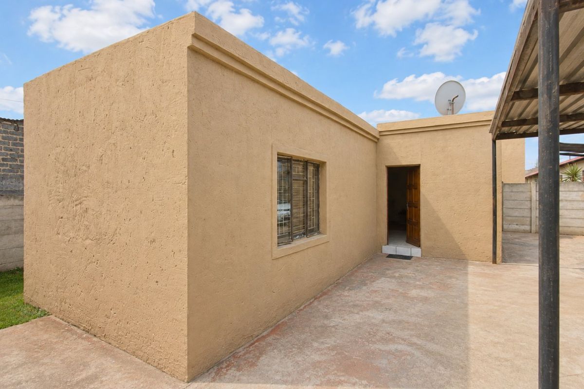 Rear exterior view of the property featuring a textured plaster facade, concrete patio area, and a covered outdoor structure.