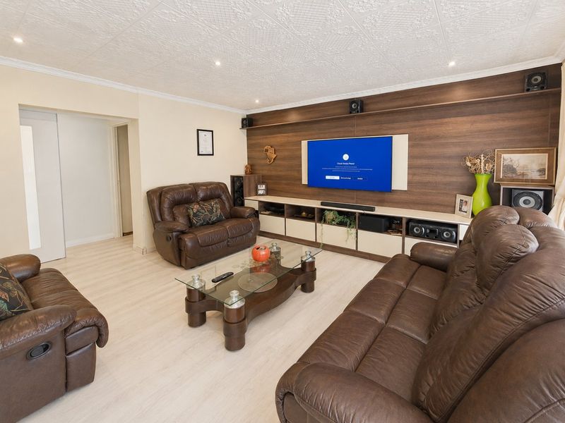 Spacious living room featuring a modern built-in media wall unit, recessed downlighting, and light-toned laminate flooring.