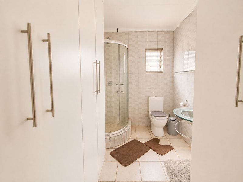 A functional bathroom featuring a curved glass shower enclosure, built-in storage cabinetry, and a glass vessel sink with neutral ceramic tiling throughout.