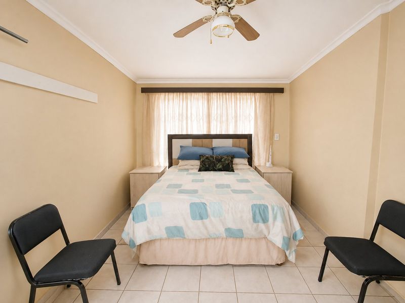 A functional bedroom featuring tiled flooring, a ceiling fan, and a window with curtain rails and security gate.